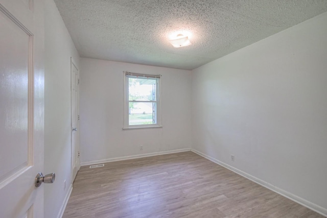 empty room featuring baseboards, visible vents, light wood-style flooring, and a textured ceiling