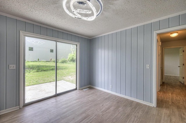 unfurnished room featuring baseboards, a textured ceiling, ornamental molding, and wood finished floors