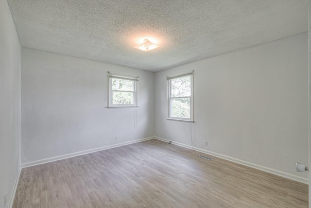 unfurnished room featuring a textured ceiling, light wood finished floors, visible vents, and baseboards