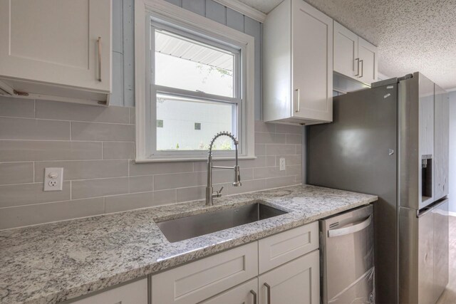 kitchen with backsplash, appliances with stainless steel finishes, white cabinets, a sink, and light stone countertops