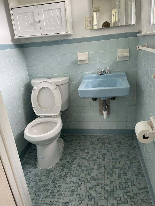 bathroom with toilet, tile walls, a sink, and tile patterned floors