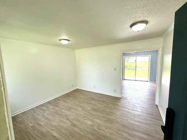 empty room with ornamental molding, a textured ceiling, baseboards, and wood finished floors