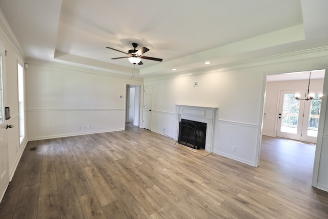 unfurnished living room with ceiling fan with notable chandelier, light wood-type flooring, and a tray ceiling