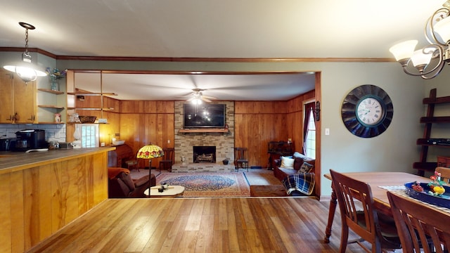 living room with a stone fireplace, ceiling fan with notable chandelier, hardwood / wood-style floors, and ornamental molding