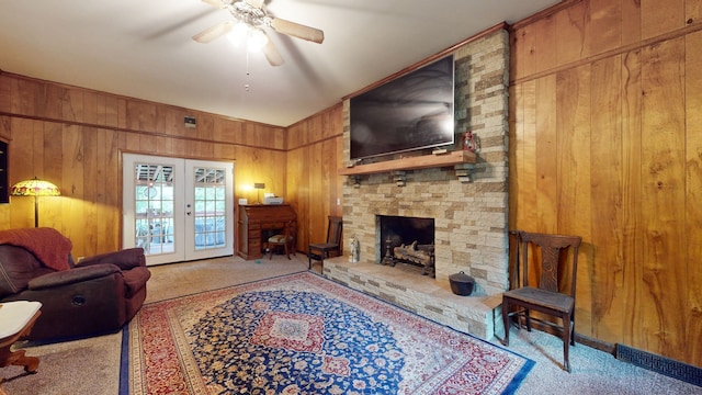 carpeted living room featuring french doors, a fireplace, ceiling fan, and wooden walls