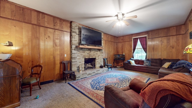 living room with a stone fireplace, wood walls, carpet, and ceiling fan