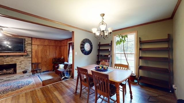 dining room featuring ceiling fan with notable chandelier, wood walls, a fireplace, hardwood / wood-style flooring, and ornamental molding