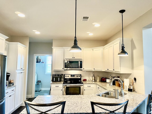 kitchen with appliances with stainless steel finishes, pendant lighting, white cabinetry, sink, and light stone countertops