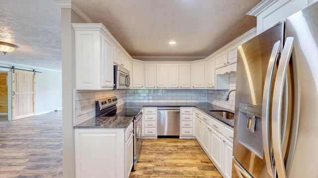 kitchen featuring sink, white cabinetry, dark stone countertops, stainless steel appliances, and light wood-type flooring