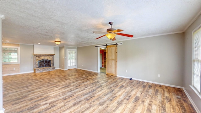 unfurnished living room featuring a fireplace, hardwood / wood-style flooring, ornamental molding, a barn door, and a textured ceiling