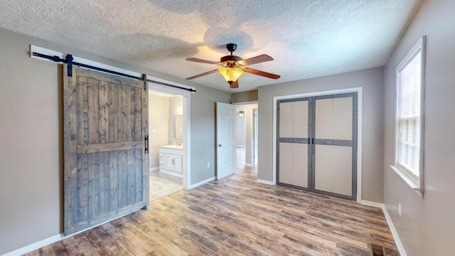 unfurnished bedroom featuring light hardwood / wood-style flooring, ceiling fan, a barn door, ensuite bath, and a closet