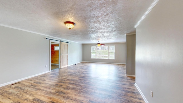 empty room featuring ornamental molding, a barn door, hardwood / wood-style floors, and a textured ceiling