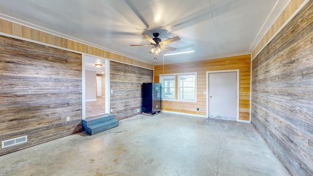 unfurnished living room featuring wooden walls, ceiling fan, and concrete flooring