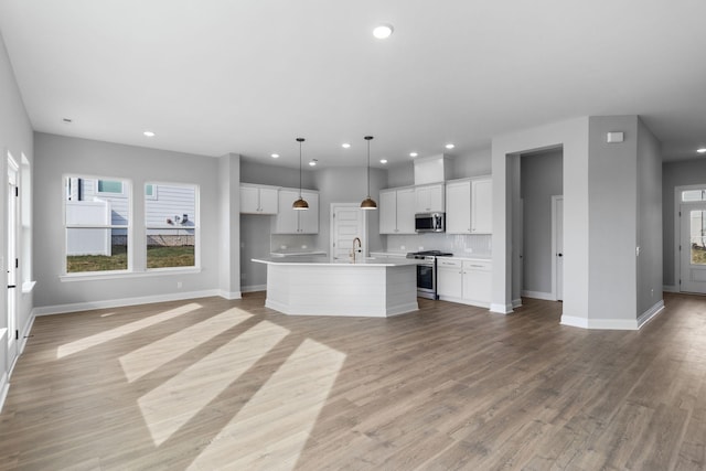 kitchen featuring a center island with sink, light wood finished floors, appliances with stainless steel finishes, open floor plan, and white cabinetry