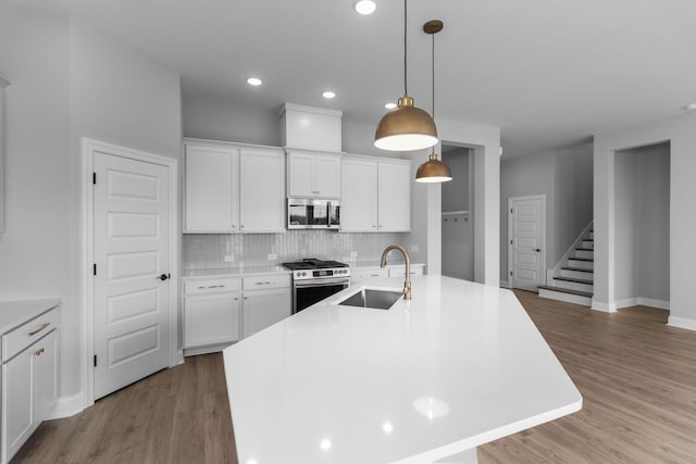 kitchen featuring wood finished floors, a sink, appliances with stainless steel finishes, decorative backsplash, and an island with sink