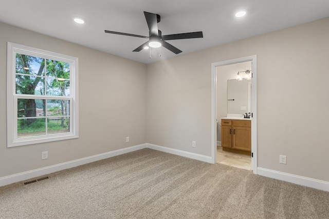 unfurnished bedroom with multiple windows, connected bathroom, light colored carpet, and ceiling fan