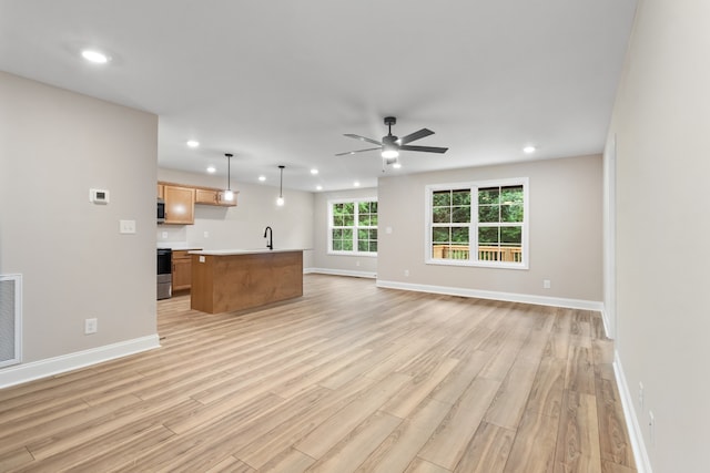 unfurnished living room featuring sink, light wood-type flooring, and ceiling fan