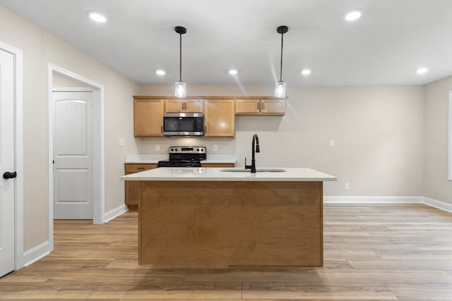 kitchen featuring appliances with stainless steel finishes, sink, pendant lighting, light wood-type flooring, and an island with sink