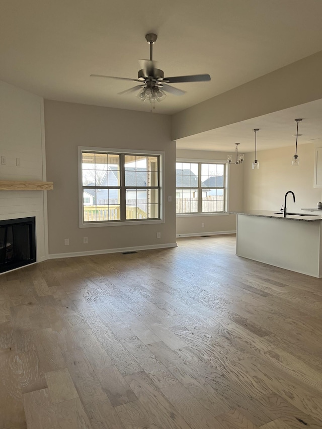 unfurnished living room featuring hardwood / wood-style floors, ceiling fan, a large fireplace, and sink