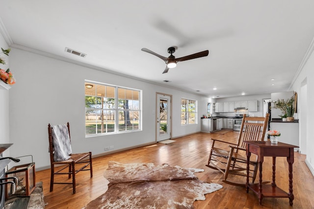 living room with baseboards, visible vents, ceiling fan, crown molding, and light wood-type flooring