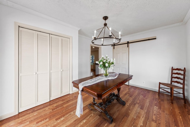 dining area with light wood finished floors, a barn door, a textured ceiling, and ornamental molding