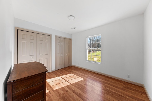 unfurnished bedroom with light wood-style floors, visible vents, baseboards, and two closets