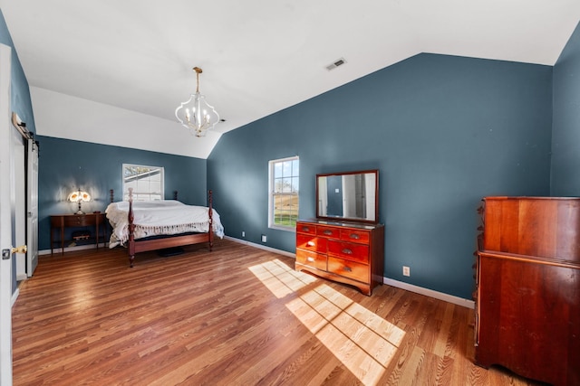 bedroom featuring lofted ceiling, a barn door, wood finished floors, and visible vents