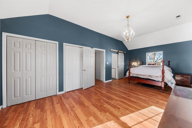 bedroom featuring light wood-type flooring, vaulted ceiling, and two closets