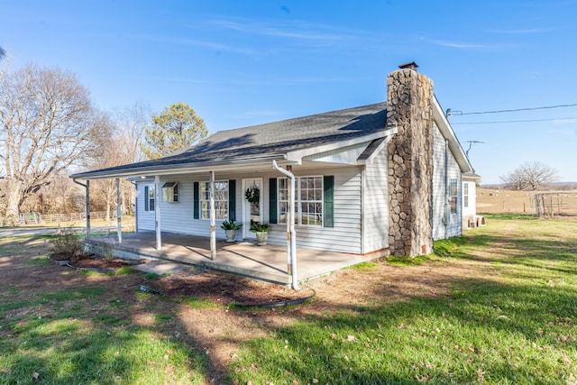 view of front facade featuring covered porch, a shingled roof, a chimney, and a front yard