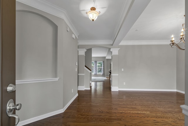 foyer featuring decorative columns, crown molding, dark wood-type flooring, and a notable chandelier