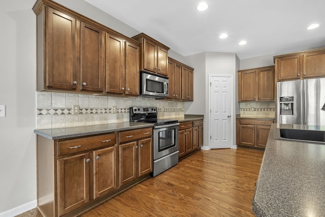 kitchen with sink, appliances with stainless steel finishes, backsplash, dark hardwood / wood-style flooring, and dark stone counters