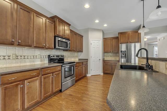 kitchen featuring sink, tasteful backsplash, hanging light fixtures, light wood-type flooring, and stainless steel appliances