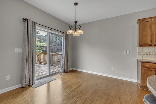 unfurnished dining area with an inviting chandelier and light wood-type flooring