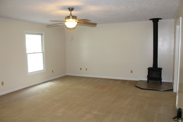 unfurnished living room featuring ceiling fan, a wood stove, ornamental molding, light colored carpet, and a textured ceiling