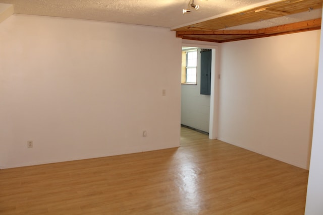 spare room with beam ceiling, a textured ceiling, and light wood-type flooring
