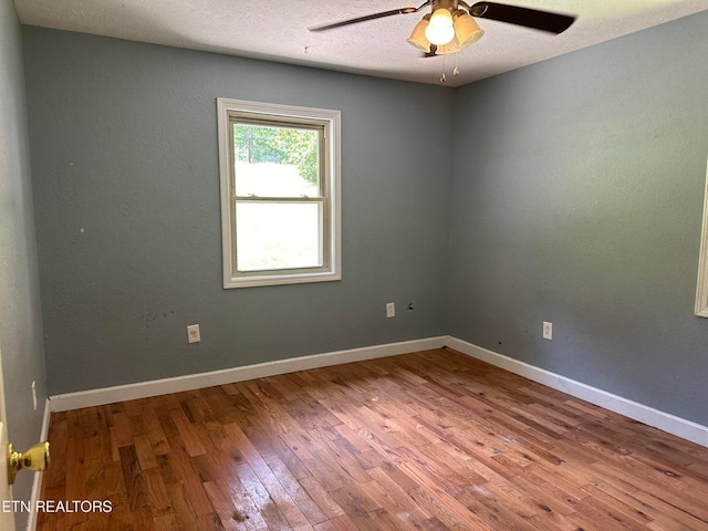 empty room with a textured ceiling, baseboards, ceiling fan, and wood finished floors