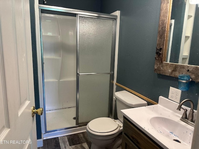 bathroom with toilet, a shower with door, wood finished floors, and vanity