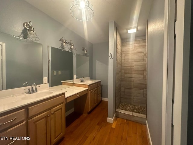 bathroom featuring two vanities, a sink, wood finished floors, tiled shower, and baseboards