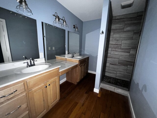 bathroom featuring baseboards, a tile shower, wood finished floors, and vanity