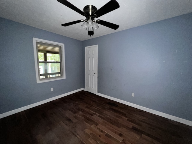 spare room with dark wood-type flooring, ceiling fan, and baseboards