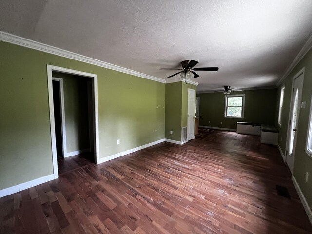 empty room with a textured ceiling, dark wood-type flooring, visible vents, baseboards, and ornamental molding