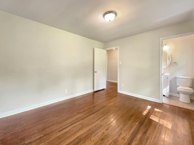 unfurnished bedroom featuring ensuite bathroom and dark hardwood / wood-style flooring