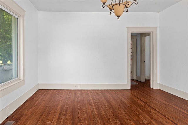 spare room with dark hardwood / wood-style floors and an inviting chandelier