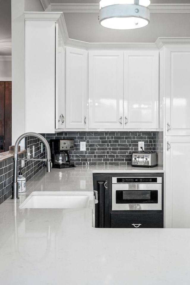 kitchen with stainless steel oven, decorative backsplash, and white cabinets