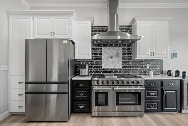 kitchen featuring stainless steel appliances, white cabinets, wall chimney range hood, decorative backsplash, and light wood-type flooring