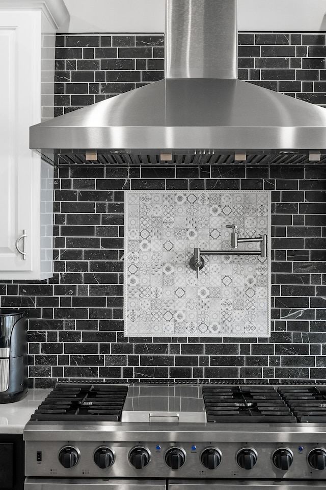 interior space featuring tasteful backsplash, white cabinets, and wall chimney range hood