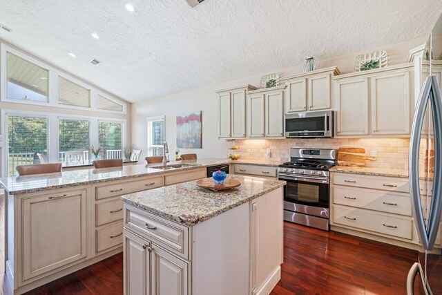 kitchen with appliances with stainless steel finishes, dark hardwood / wood-style flooring, vaulted ceiling, and a kitchen island