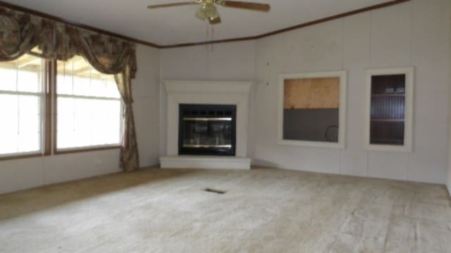 unfurnished living room with light colored carpet, ceiling fan, and crown molding