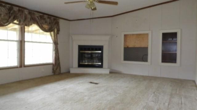 unfurnished living room featuring crown molding, ceiling fan, and carpet