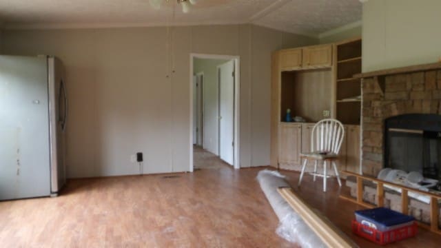 living room featuring a textured ceiling, ceiling fan, crown molding, light hardwood / wood-style flooring, and a fireplace